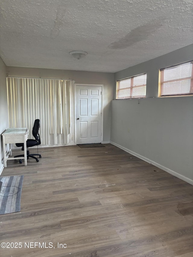 unfurnished office featuring a textured ceiling, wood finished floors, and baseboards