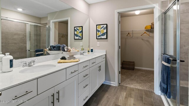 bathroom featuring a walk in closet, a stall shower, double vanity, and a sink