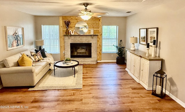 living room featuring baseboards, wood finished floors, a ceiling fan, and a brick fireplace