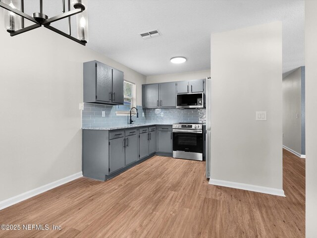 1615 Brook Forest Dr, Jacksonville, FL 32208 - kitchen with light wood-style floors, tasteful backsplash, baseboards, gray cabinetry, and appliances with stainless steel finishes