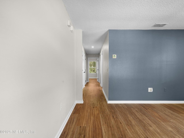 corridor featuring a textured ceiling, visible vents, wood finished floors, and baseboards