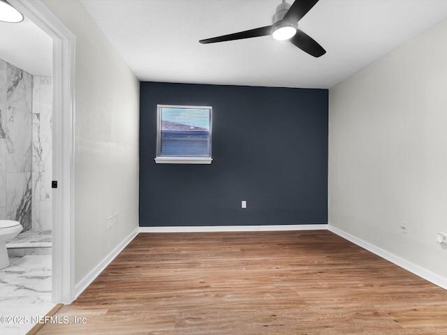 interior space with baseboards, wood finished floors, a ceiling fan, and ensuite bathroom