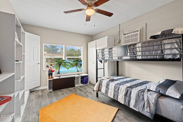 bedroom with ceiling fan, a wall mounted AC, and wood finished floors