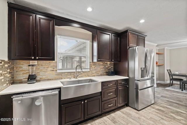 kitchen with dark brown cabinets, appliances with stainless steel finishes, a sink, decorative backsplash, and ornamental molding