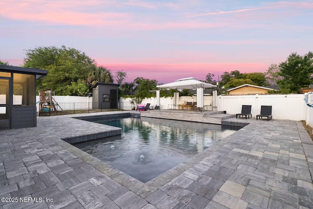 pool at dusk with a patio, a fenced in pool, a fenced backyard, and a playground