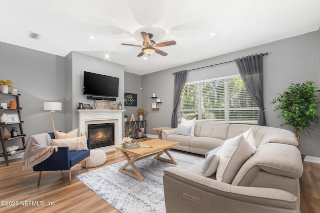 living area with light wood-style floors, a glass covered fireplace, a ceiling fan, visible vents, and baseboards