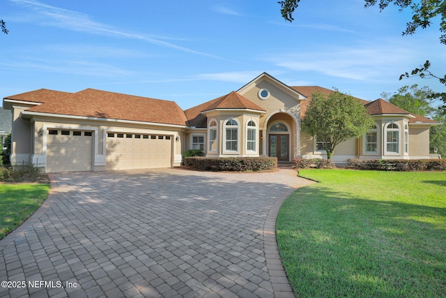 view of front facade featuring a garage, a front yard, decorative driveway, stucco siding, and french doors