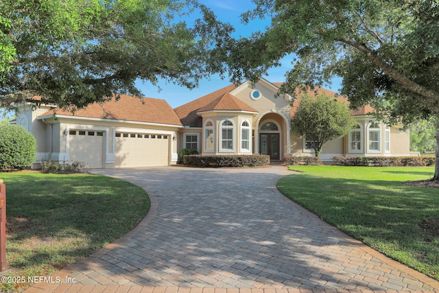 mediterranean / spanish home featuring a garage, stucco siding, a front yard, decorative driveway, and french doors