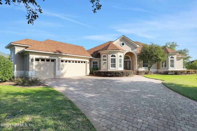 view of front of property with an attached garage, stucco siding, decorative driveway, and a front yard