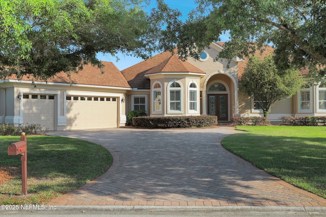 mediterranean / spanish-style home featuring an attached garage, a front lawn, stucco siding, decorative driveway, and french doors
