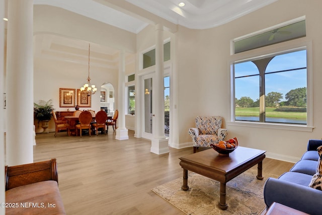 living area featuring a chandelier, baseboards, decorative columns, wood finished floors, and ornamental molding