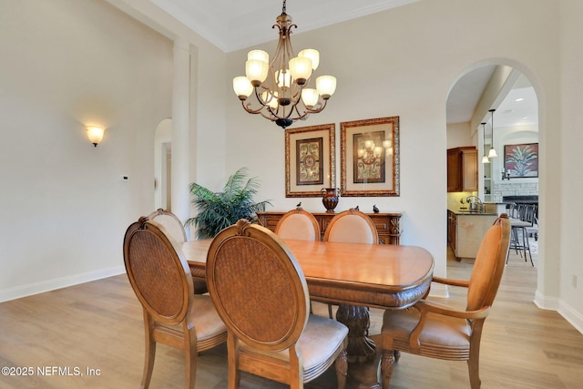 dining area with a fireplace, baseboards, light wood-type flooring, arched walkways, and a notable chandelier