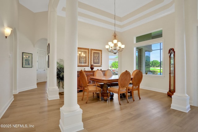 dining room with a high ceiling, a notable chandelier, light wood finished floors, arched walkways, and ornate columns