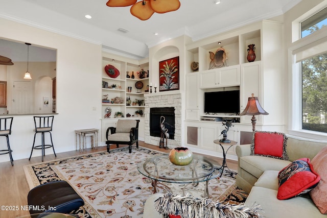 living area with crown molding, ceiling fan, wood finished floors, and built in shelves