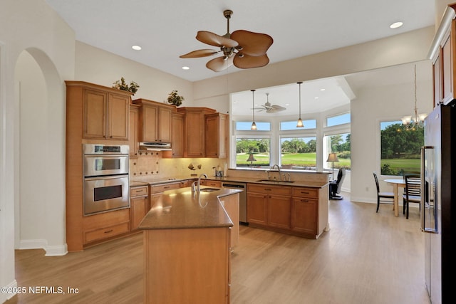 kitchen with light wood finished floors, appliances with stainless steel finishes, a kitchen island with sink, and ceiling fan