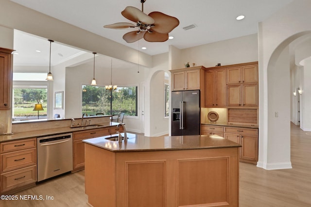 kitchen with light wood-type flooring, arched walkways, a sink, and appliances with stainless steel finishes