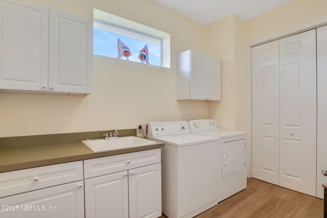 clothes washing area with a sink, light wood-style floors, washing machine and dryer, and cabinet space