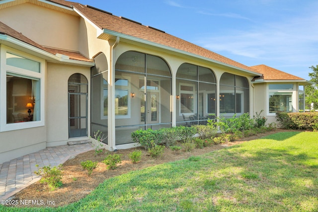 rear view of property featuring a lawn, stucco siding, and a sunroom