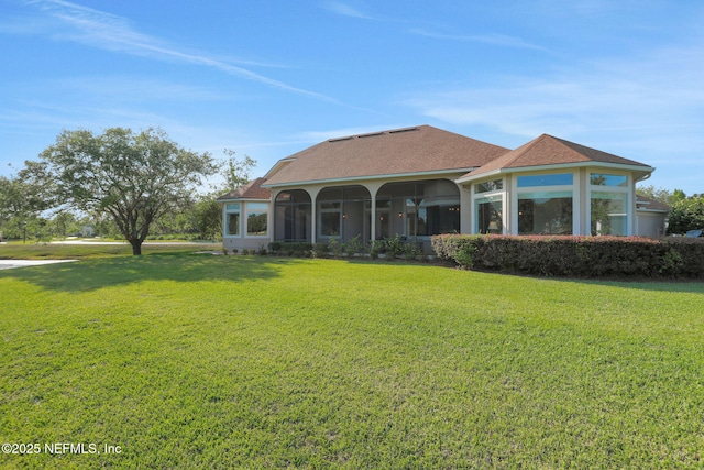 rear view of house featuring a sunroom, a lawn, and roof with shingles
