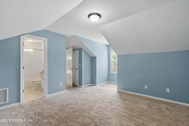 additional living space with carpet floors, a textured ceiling, baseboards, lofted ceiling, and visible vents