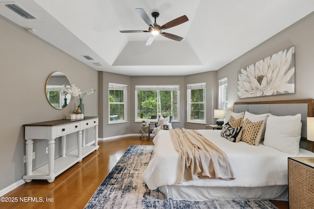bedroom with baseboards, visible vents, wood finished floors, and a raised ceiling