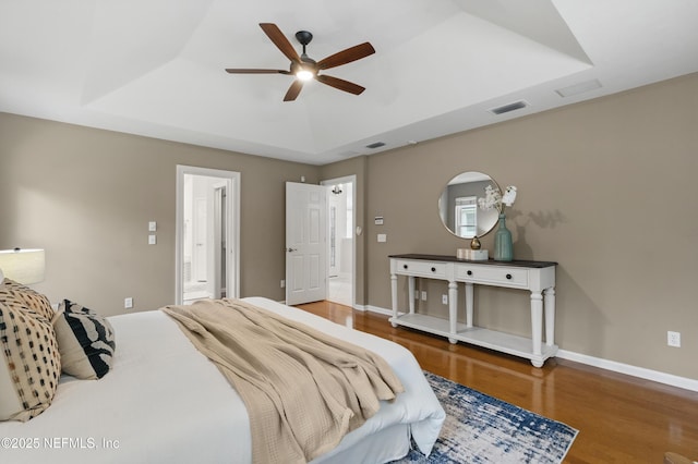 bedroom featuring ceiling fan, baseboards, wood finished floors, a tray ceiling, and visible vents
