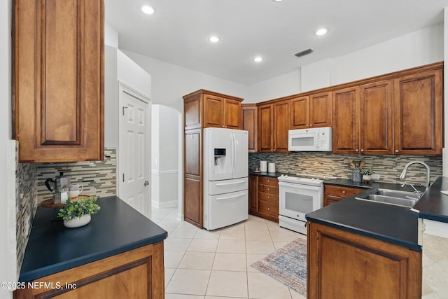 kitchen featuring visible vents, dark countertops, white appliances, tasteful backsplash, and a sink