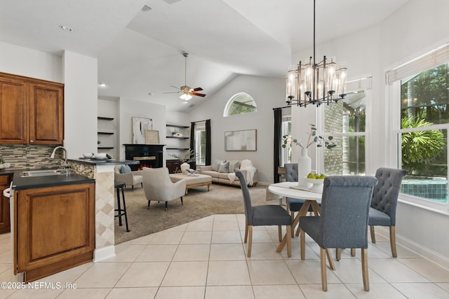 dining space with a warm lit fireplace, ceiling fan with notable chandelier, light tile patterned flooring, and a healthy amount of sunlight