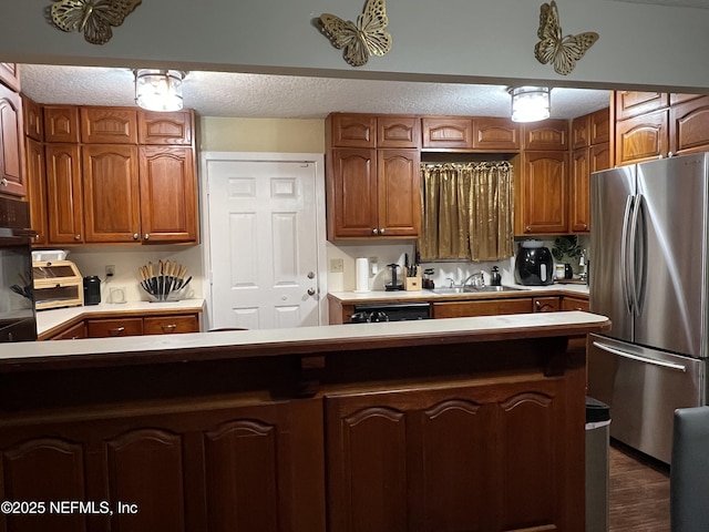 kitchen featuring brown cabinetry, a textured ceiling, light countertops, and freestanding refrigerator