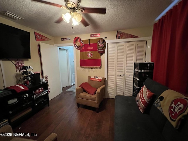 living room with dark wood finished floors, visible vents, a ceiling fan, and a textured ceiling