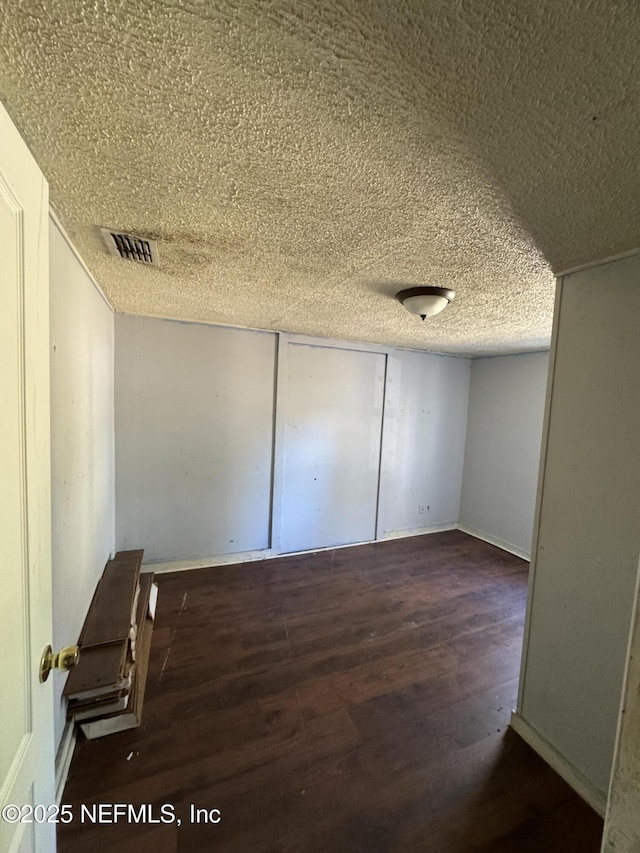 empty room featuring baseboards, visible vents, wood finished floors, and a textured ceiling