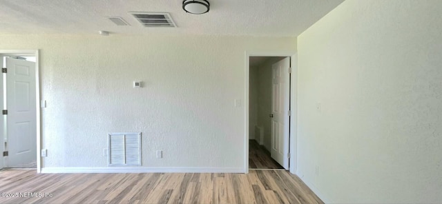 empty room with baseboards, visible vents, and light wood finished floors