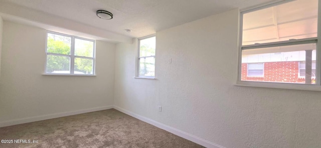 spare room featuring a textured wall, carpet, and baseboards