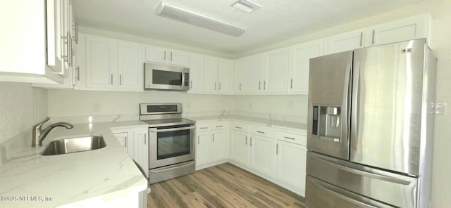 kitchen featuring light stone countertops, appliances with stainless steel finishes, white cabinets, a sink, and visible vents