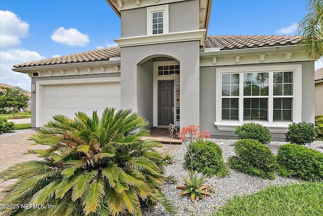 doorway to property featuring stucco siding, driveway, a tiled roof, and an attached garage