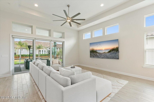 living room with a raised ceiling, ceiling fan, light wood finished floors, and plenty of natural light
