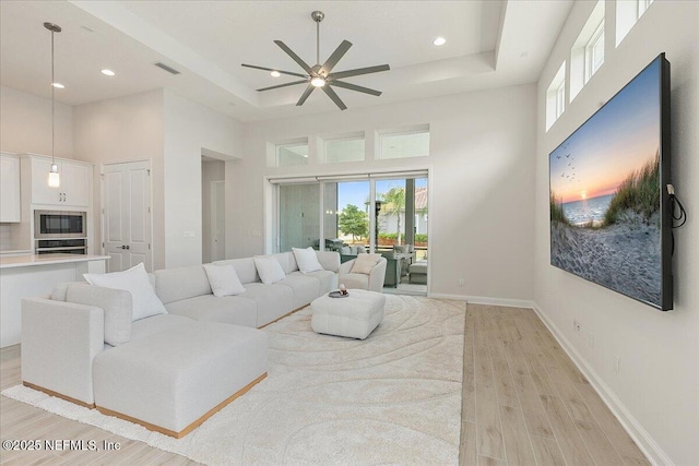 living area with light wood-style floors, visible vents, a raised ceiling, a ceiling fan, and a towering ceiling