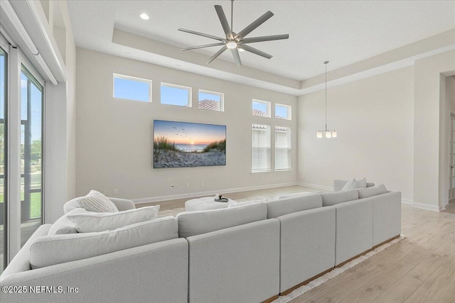 living room with baseboards, light wood-type flooring, ceiling fan with notable chandelier, and plenty of natural light