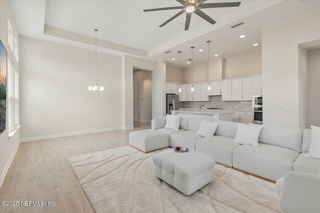 living area featuring recessed lighting, light wood-style floors, ceiling fan with notable chandelier, baseboards, and visible vents