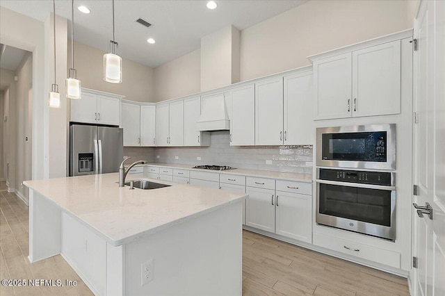 kitchen featuring tasteful backsplash, light stone countertops, stainless steel appliances, a sink, and light wood-type flooring