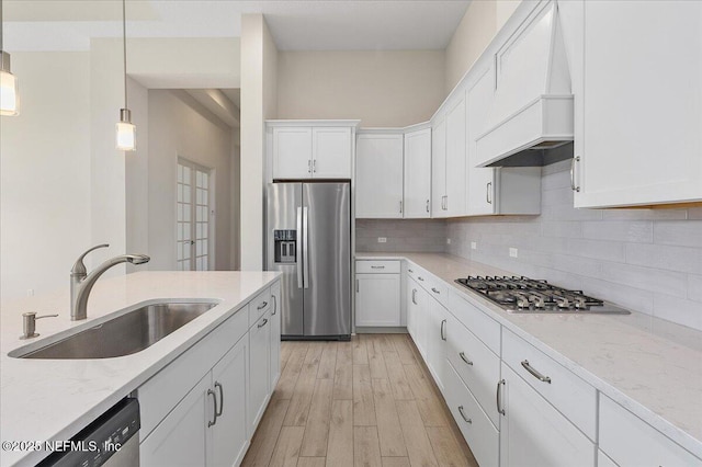 kitchen featuring a sink, stainless steel appliances, backsplash, white cabinetry, and premium range hood