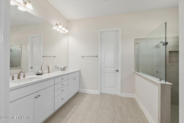 full bath featuring double vanity, walk in shower, baseboards, and a sink