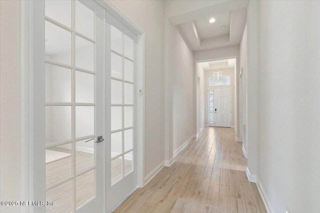 hall with light wood-type flooring, a tray ceiling, and baseboards