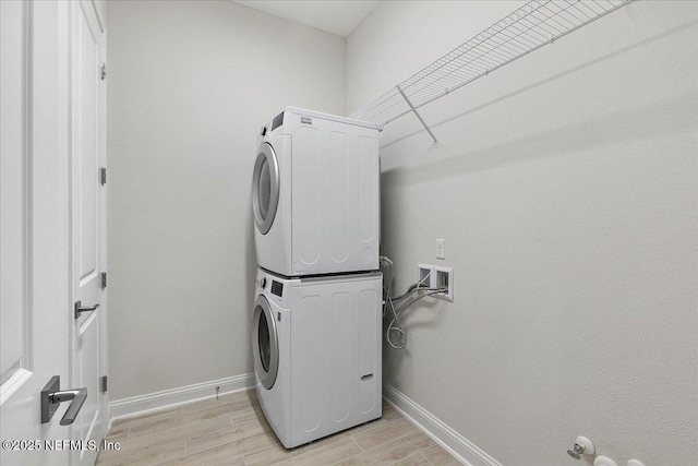 washroom with stacked washer and clothes dryer, light wood-style flooring, laundry area, and baseboards