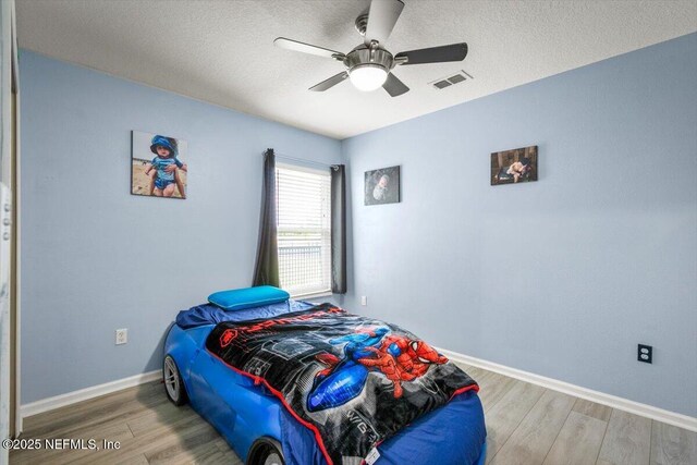 bedroom with a textured ceiling, baseboards, wood finished floors, and visible vents