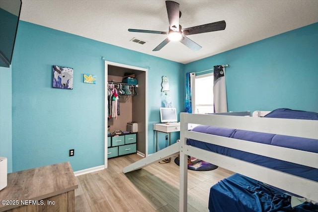 bedroom featuring ceiling fan, visible vents, wood finished floors, baseboards, and a closet