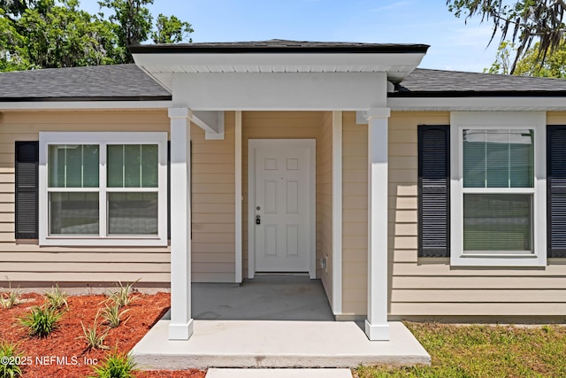 view of exterior entry featuring covered porch and a shingled roof