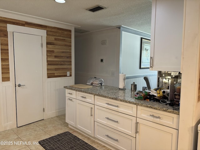 interior space featuring stone counters, a wainscoted wall, visible vents, white cabinetry, and a textured ceiling