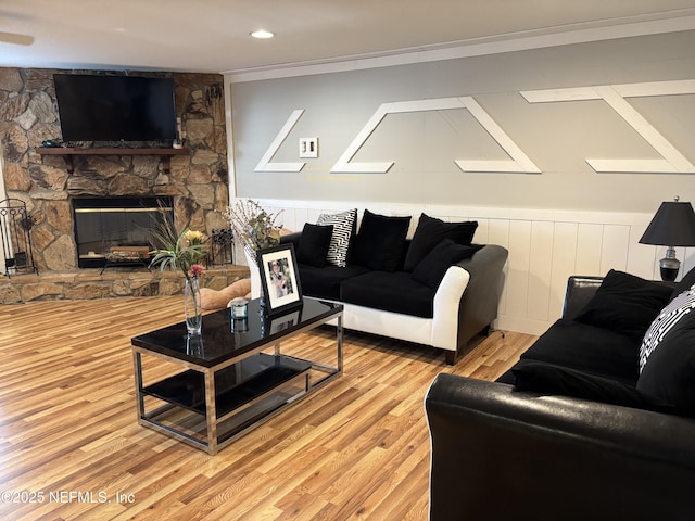 living area featuring crown molding, light wood-style flooring, and a stone fireplace
