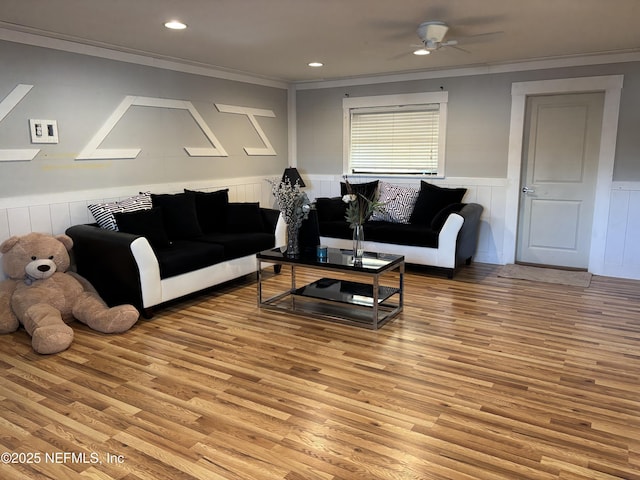 living room with ceiling fan, light wood-type flooring, crown molding, and wainscoting